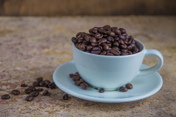 Spilled coffee beans from the white ceramic cup on the wooden ba