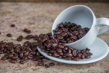 Spilled coffee beans from the white ceramic cup on the wooden ba