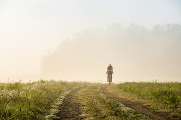Fototapeta premium Small silhouette of man on bicycle in misty november active morning