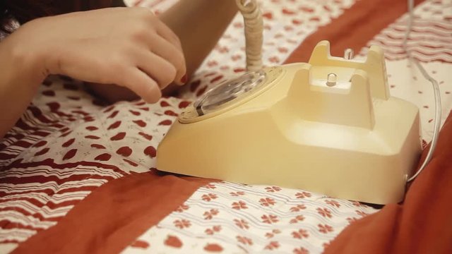 A female hand dialling a number on a vintage retro rotary telephone.
