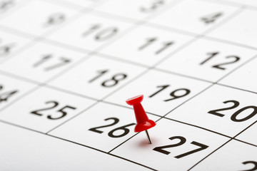Pin on the date number 27. The twenty seventh day of the month is marked with a red thumbtack. Focus point on the red pin.