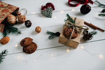 Christmas gift box is packed in kraft paper. Christmas gift decorated: fir sprigs, cookies, pine cone and Christmas lights. Christmas concept.