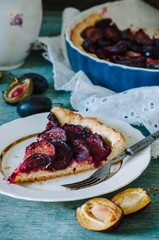 Homemade pie with plums on the blue wooden background table. Baked and raw plums.