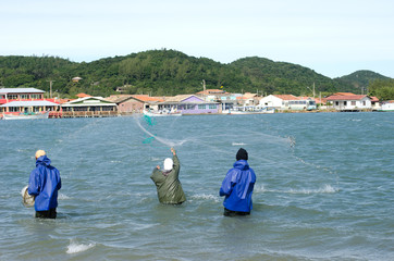 Three working fishermen one is playing the net in a Laguna's beach Santa Catarina Brazil