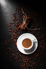 Fresh tasty espresso cup of hot coffee with coffee beans on dark