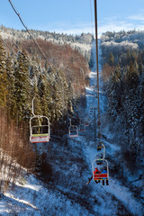 Winter mountain lift for skiers above snowy forest and sky