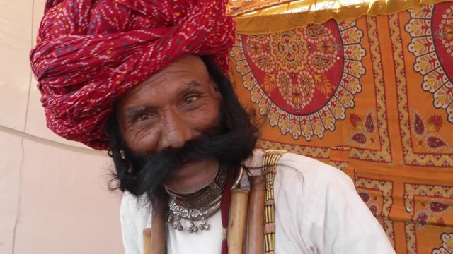 Smiling man from Rajasthan salutes with big moustache wearing a red turban and tradition dress