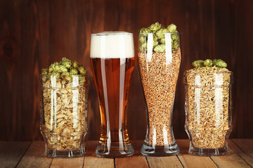 Glasses with beer, hops and malts on wooden background