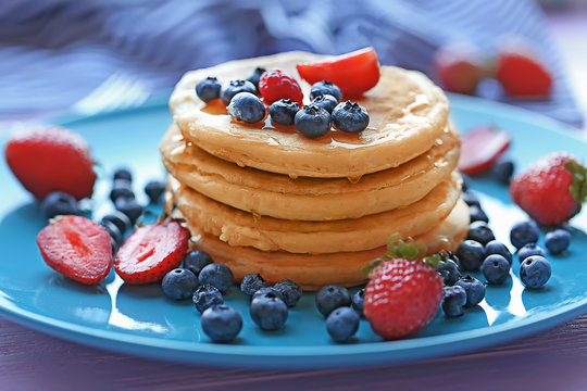 Tasty pancakes with berries on blue plate, close up view