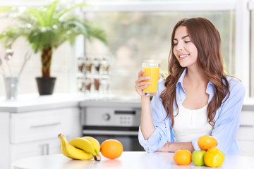 Beautiful young woman with glass of orange juice sitting at kitchen table