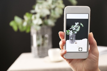 Woman taking photo of green eucalyptus branches in vase