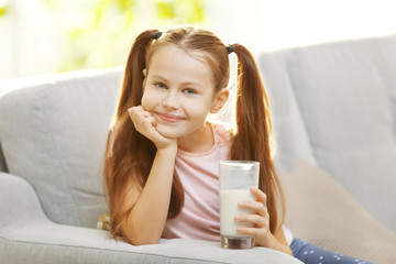 Cute little girl with glass of fresh milk on couch