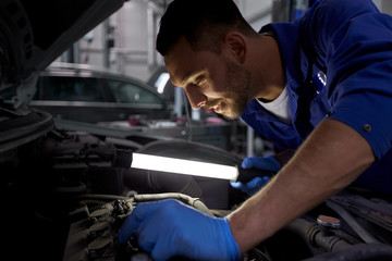 mechanic man with lamp repairing car at workshop