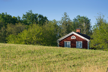 Old traditional red painted farmhouse in Sweden hidden behind hills. In the foreground landscape with meadows