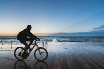 Silhouette of a man riding a bicycle on a pier at sunset