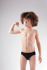 Curly boy in shorts bent arm at the elbow. He looks into the camera. White background.