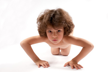 Curly boy in shorts kneeling on the floor leaning hands. He looks into the camera. White background.