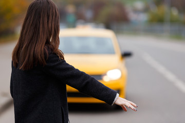Portrait from the back of brunette woman stopping yellow taxi