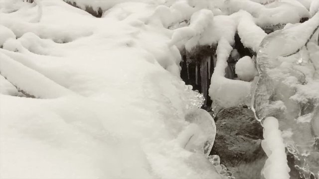 slow motion of stream through snow in winter forest
