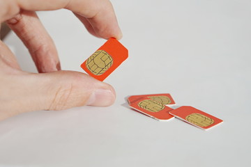Isolated photo of male hand holding red SIM card above a group of 3 other SIM cards used in the mobile phones (cell phone devices) with a focus on their golden micro chip 