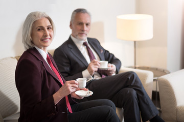 Delighted businesswoman drinking coffee with her colleague