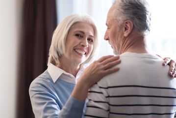Delighted aged couple hugging each other at home