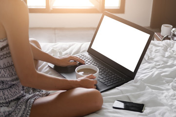 Young lady freelancer sitting on the bed in hotel room in front of window and working in laptop....