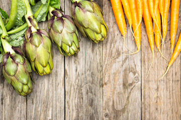 Fresh artichokes and carrots on old wood top view image with copy space for text