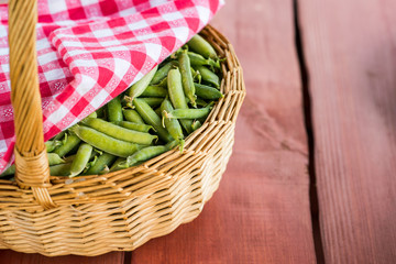 Unopened pea pods in a basket on wooden background.