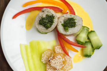 Fish rolls wrapped in zucchini with roasted potatoes sprinkled with sesame seeds and slices of bell pepper and cucumber. Wooden rustic background. Top view. Close-up