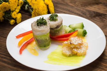 Fish rolls wrapped in zucchini with roasted potatoes sprinkled with sesame seeds and slices of bell pepper and cucumber. Wooden rustic background. Top view. Close-up