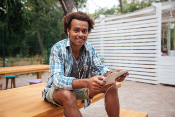 Fototapeta premium Cheerful african young man listening to music from tablet