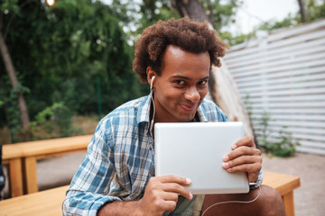 Fototapeta premium Smiling cute african young man with tablet listening to music