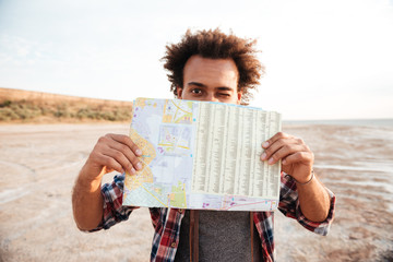 Joyful african man covered his face with map and winking