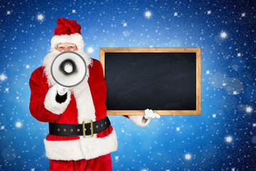 Santa claus megaphone holding empty wooden blackboard and pointing with his finger in front of blue...