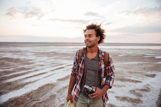 Happy man with backpack and vintage camera walking on beach