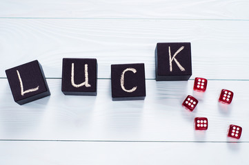 Luck word written in black wooden cubes and red dice on a blue wooden background, flat lay. Concept for business risk, chance, good luck or gambling, top view.