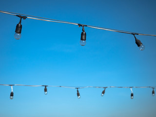 Light bulbs hanging on electric wires with blue sky background