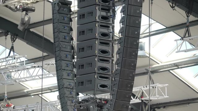 Lots of black amplifiers hanging on the ceiling of a concert stage with other wires in Ireland