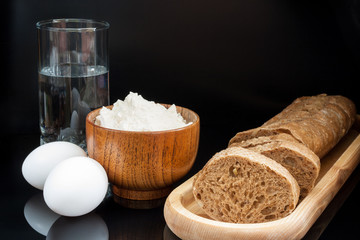 Flour, eggs, glass of water with fresh sliced baguette on black 