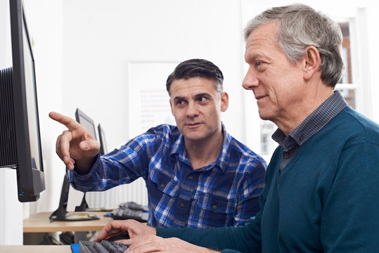 Tutor Helping Mature Man In Computer Class