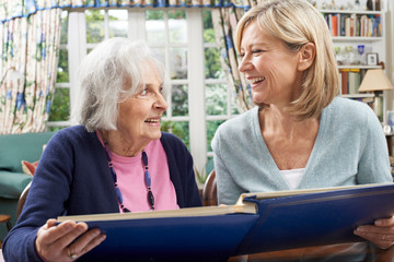 Senior Woman Looks At Photo Album With Mature Female Neighbor