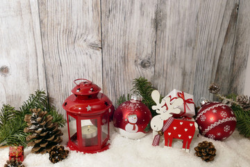 Weihnachtliche Dekoration aus roter Laterne, Weihnachtskugeln, Elchfigur, Tannengrün und Tannenzapfen vor einer Holzwand