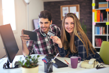 Couple of web designers working together at modern office, using credit card