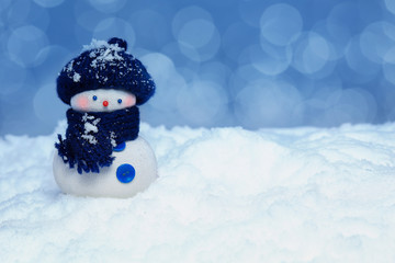 snowman wearing a knitted blue beret  and scarf. Behind him, the snow blurred background. The...