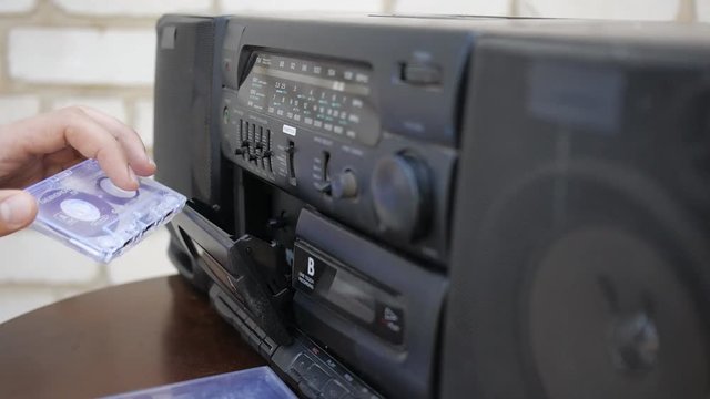 The man inserts the audio cassette into the outdated tape recorder. Close-up.