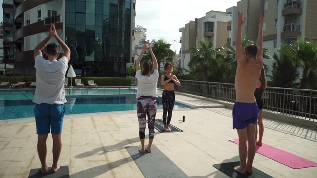 group of people practicing yoga next to the swimming pool slow motion