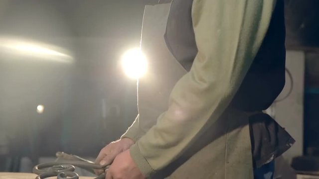 The blacksmith puts on the table forged metal product in the form of heart
