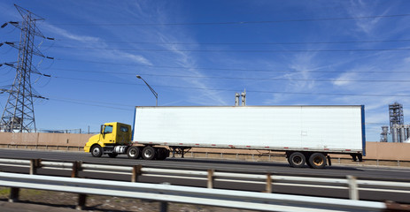 Yellow cab semi with white trailer on interstate under blue sky. Horizontal.