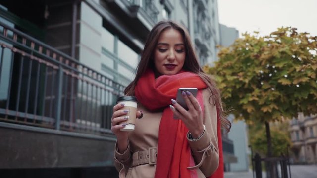 Attractive European brunette girl with red lipstick, long hair and stylish look. A business lady tapping the message on her phone, and has a coffee break in the city center.